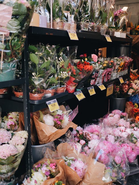 A display of fresh flowers inside a flower shop, featuring an assortment of vibrant blooms including pink peonies, white hydrangeas, and red roses arranged in bouquets and wrapped in brown craft paper