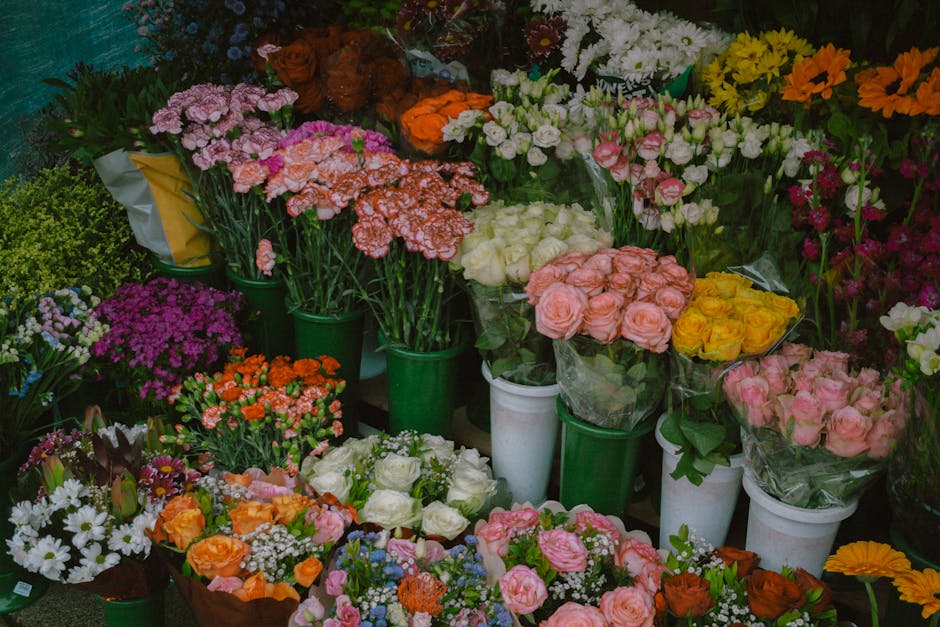 A vibrant display of fresh floral arrangements and bouquets featuring a variety of flowers in multiple colors, including pink, white, yellow, orange, and purple, arranged in green and white buckets an