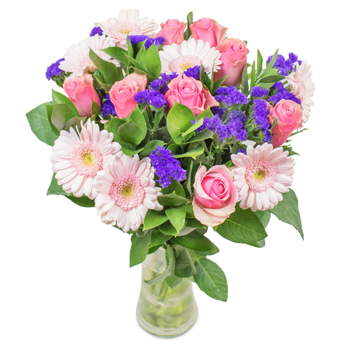 A vibrant and elegantly presented floral bouquet, perfectly suited for New Cross living, stands arranged in a clear glass vase against a simple white background. The focal point is formed by seven to nine pink roses, their petals ranging from soft blush to deeper shades, with several buds beginning to open in a classic spiral, symbolising the area's timeless charm. Around them, five to seven pale pink Gerbera daisies fan out, their round, cheerful faces and almost snowy centres brightening the composition. Clusters of bright purple statice weave through the arrangement, offering a dramatic pop of colour and delicate papery texture. Deep, lush green foliage forms a generous base, reminiscent of the greenery that borders Folkestone Gardens, enhancing both vibrancy and vitality. The transparent vase reveals the freshness of the stems and water, a detail that highlights local commitment to quality and authenticity. Suitable for birthdays, anniversaries, or as an everyday accent gracing a creative New Cross studio or home, this carefully crafted bouquet perfectly conveys celebration, affection, and a sense of renewal unique to the area. Each floral element has been thoughtfully chosen for both visual impact and heartfelt meaning, echoing the spirit of this diverse and lively SE14 community.